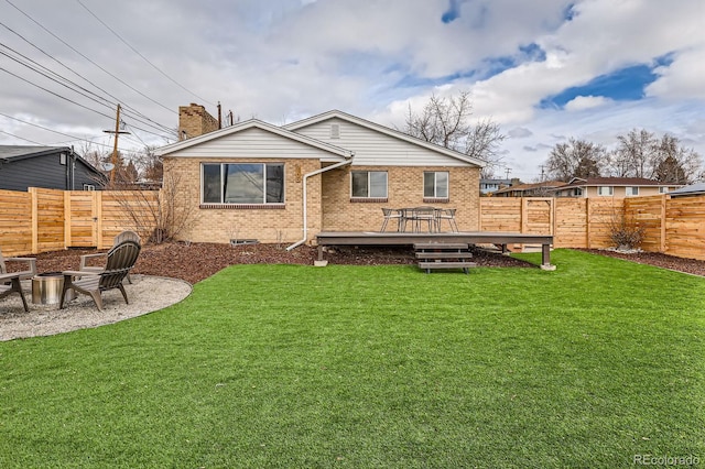 rear view of house with a fenced backyard, a fire pit, a deck, and brick siding