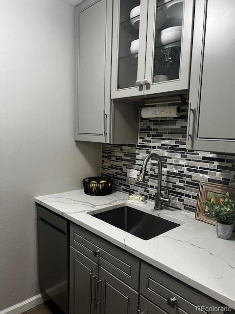 kitchen featuring gray cabinets, light stone counters, decorative backsplash, and a sink