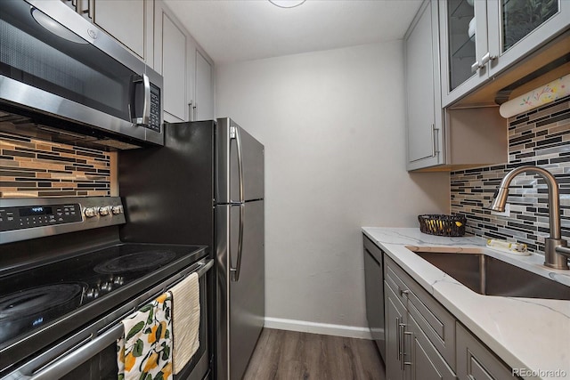 kitchen with dark wood finished floors, a sink, stainless steel appliances, gray cabinetry, and backsplash