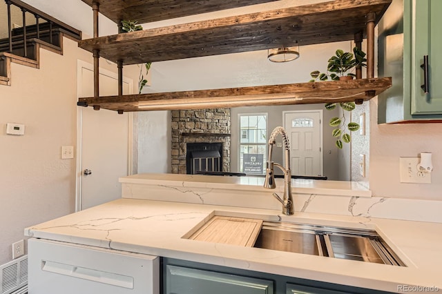 kitchen with a sink, light stone counters, visible vents, green cabinetry, and a stone fireplace