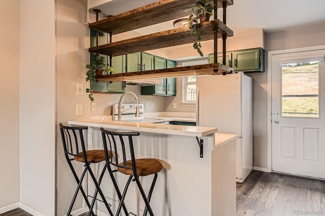 kitchen with green cabinetry, freestanding refrigerator, open shelves, a peninsula, and range