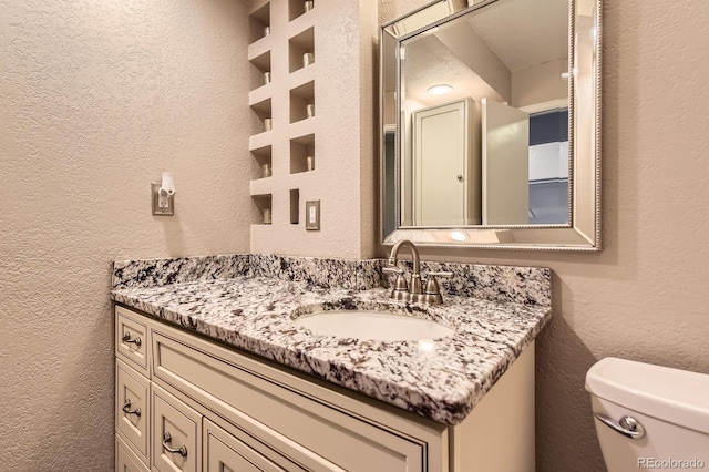 bathroom featuring a textured wall, toilet, and vanity