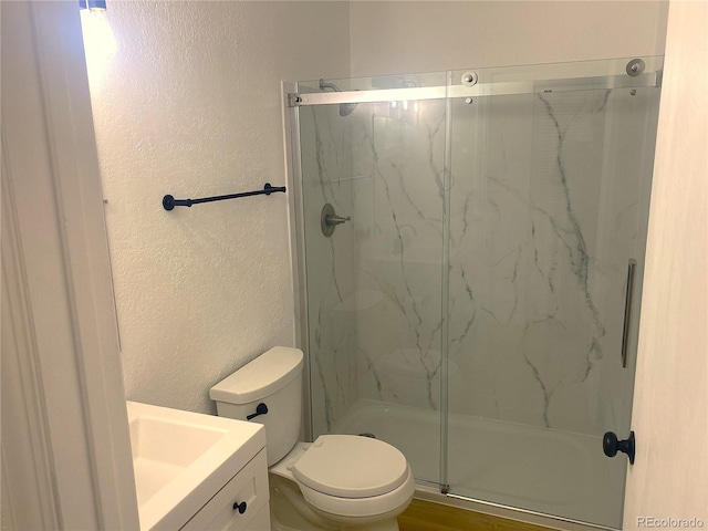 full bath with a marble finish shower, toilet, vanity, and a textured wall