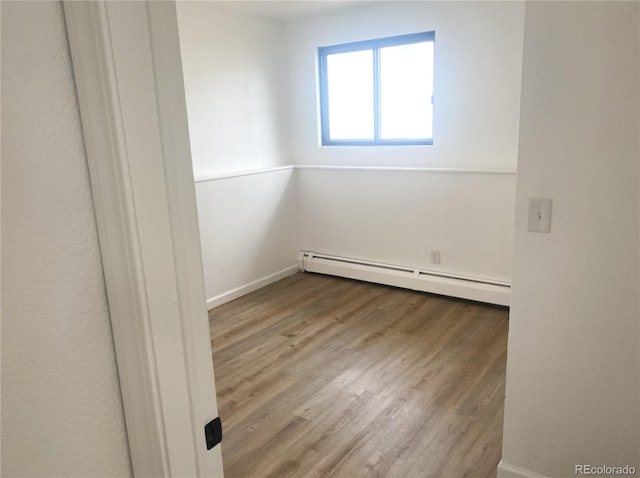 unfurnished room featuring a baseboard heating unit, baseboards, and wood finished floors