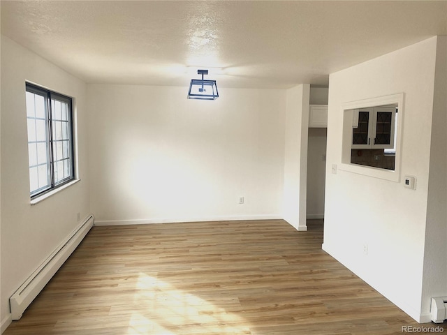 spare room featuring a textured ceiling, a baseboard heating unit, and light wood-style floors