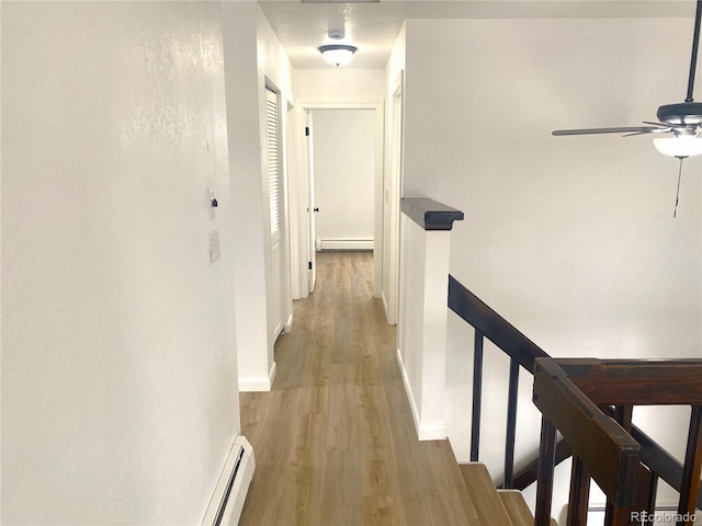 hall featuring baseboards, an upstairs landing, baseboard heating, and light wood-style flooring