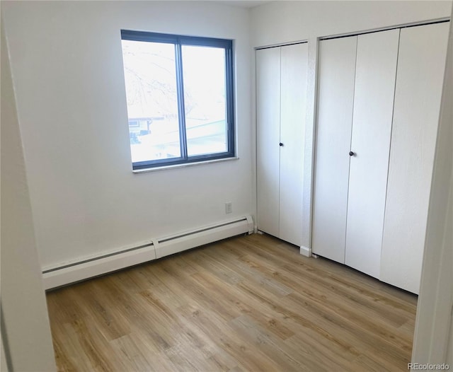 unfurnished bedroom with light wood finished floors, a baseboard heating unit, and multiple closets