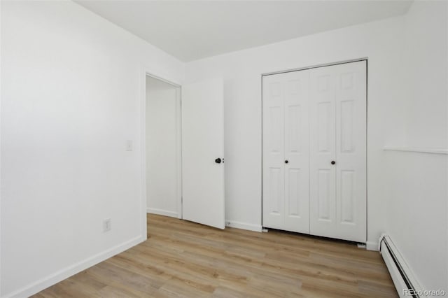 unfurnished bedroom with a closet, baseboards, light wood finished floors, and baseboard heating