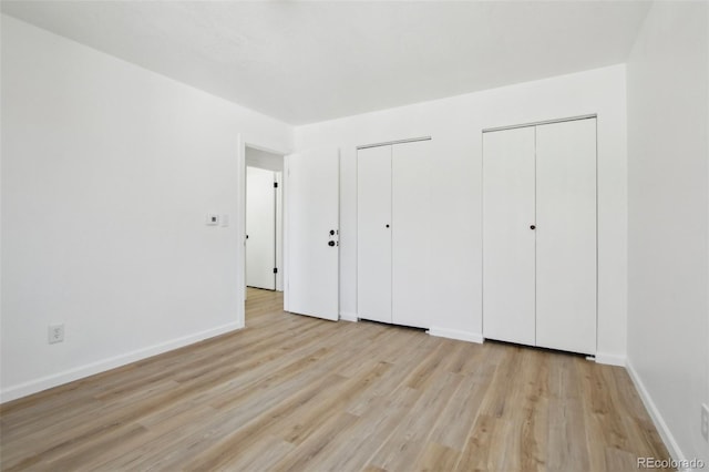 unfurnished bedroom with two closets, baseboards, and light wood-type flooring