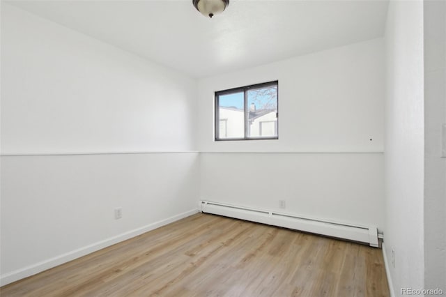spare room featuring a baseboard heating unit, baseboards, and wood finished floors