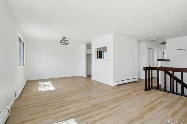 spare room featuring light wood finished floors, a baseboard heating unit, and a healthy amount of sunlight