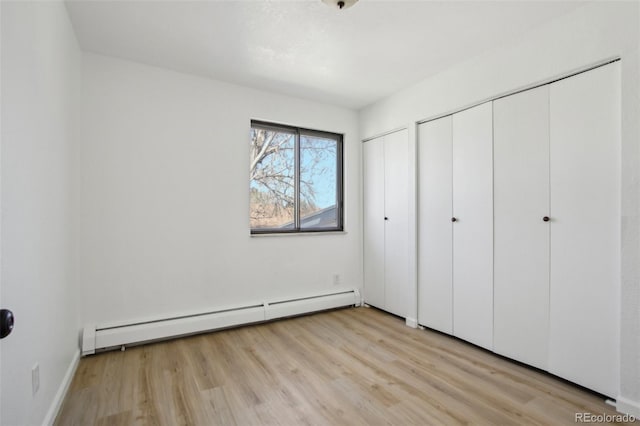unfurnished bedroom with a baseboard radiator, multiple closets, and light wood-style floors