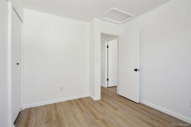 spare room with baseboards, light wood-type flooring, and attic access