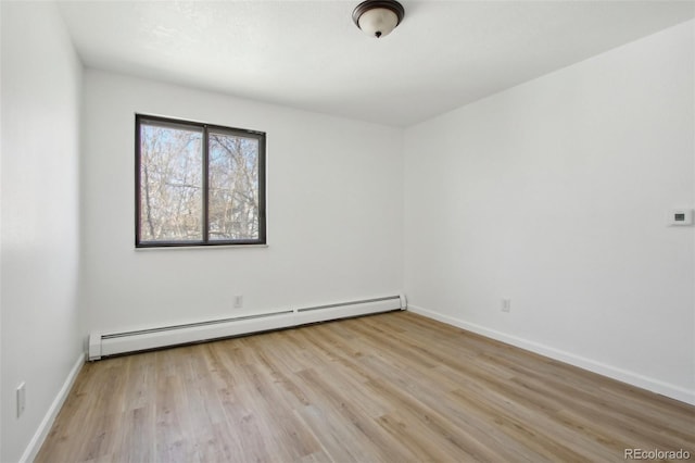 empty room with baseboard heating, light wood finished floors, and baseboards