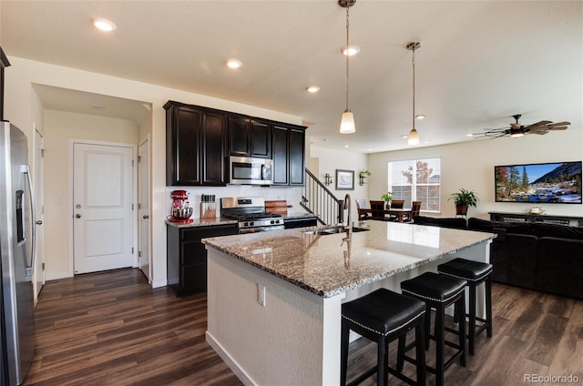 kitchen with hanging light fixtures, sink, light stone counters, a center island with sink, and stainless steel appliances