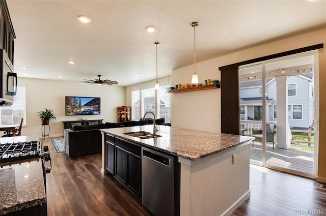 kitchen featuring appliances with stainless steel finishes, decorative light fixtures, sink, light stone counters, and a center island with sink