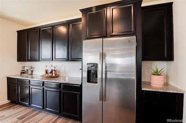 kitchen with light wood-type flooring, light stone counters, and stainless steel refrigerator with ice dispenser