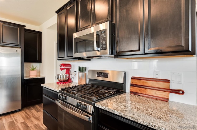 kitchen with light wood-type flooring, dark brown cabinetry, light stone countertops, and appliances with stainless steel finishes