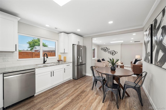 4905 W 11th Ave, Denver, CO 80204 - kitchen featuring appliances with stainless steel finishes, ornamental molding, light wood finished floors, white cabinets, and light stone countertops