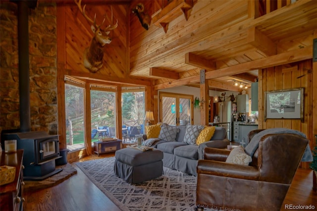 living room featuring beamed ceiling, a wood stove, a high ceiling, wooden walls, and hardwood / wood-style floors