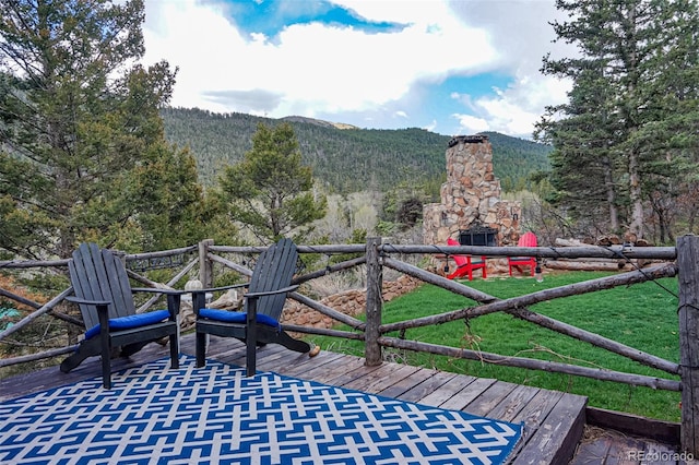 deck featuring a mountain view, a yard, and an outdoor stone fireplace