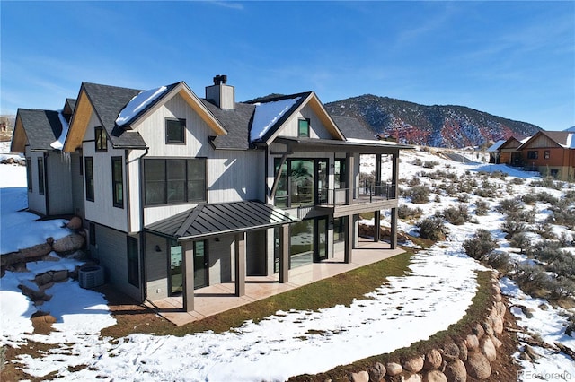 snow covered back of property featuring central AC unit, a mountain view, and a balcony