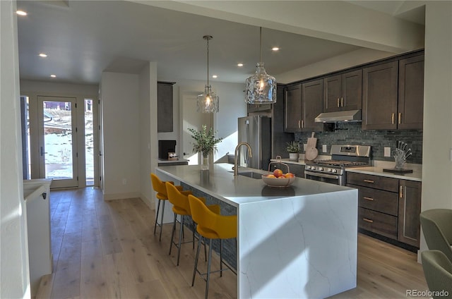 kitchen featuring dark brown cabinetry, a kitchen breakfast bar, light hardwood / wood-style flooring, a kitchen island with sink, and appliances with stainless steel finishes