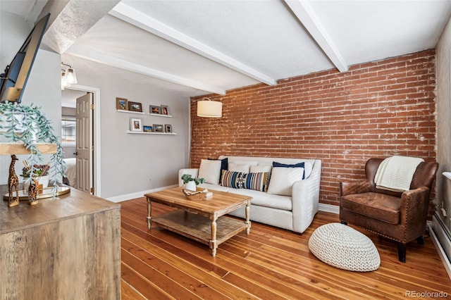 living room featuring hardwood / wood-style floors, beamed ceiling, and brick wall