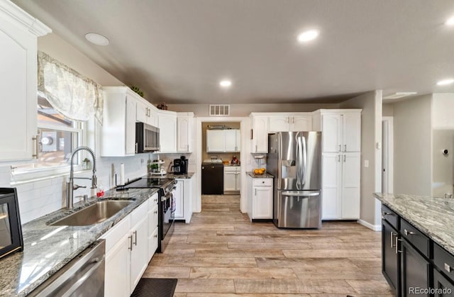 1882 N Rough Rock Ln, Pueblo West, CO 81007 - kitchen with appliances with stainless steel finishes, a sink, white cabinetry, light wood-style flooring, and washer / clothes dryer