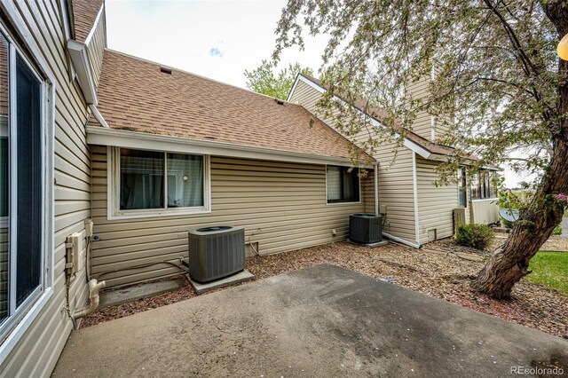 back of house featuring cooling unit, a patio, and roof with shingles
