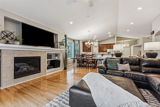 living room with light wood-type flooring, ceiling fan with notable chandelier, a fireplace, and vaulted ceiling