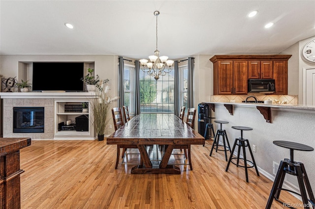 dining area featuring light hardwood / wood-style floors, a tiled fireplace, and a chandelier