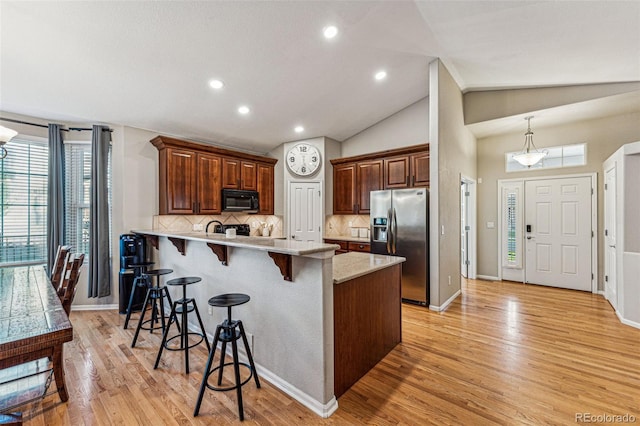 kitchen featuring light hardwood / wood-style floors, tasteful backsplash, stainless steel fridge with ice dispenser, a breakfast bar area, and vaulted ceiling