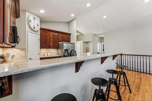 kitchen with lofted ceiling, stainless steel fridge, backsplash, a kitchen breakfast bar, and light hardwood / wood-style floors