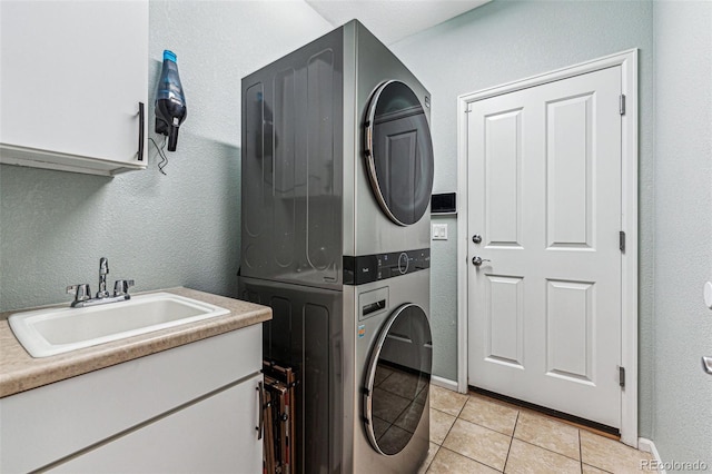 clothes washing area featuring cabinets, sink, light tile patterned floors, and stacked washer and clothes dryer