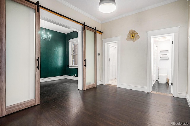 unfurnished room with a barn door, wood finished floors, baseboards, and ornamental molding