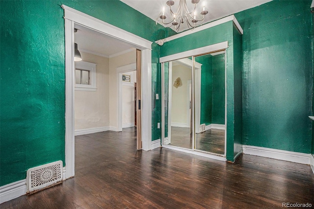 empty room with a chandelier, wood finished floors, crown molding, baseboards, and a textured wall