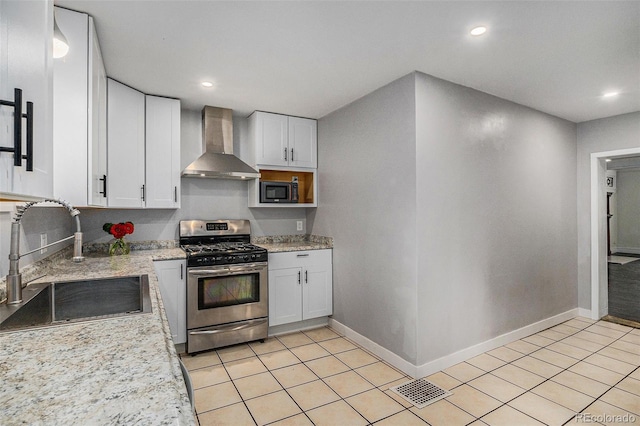 kitchen featuring appliances with stainless steel finishes, wall chimney exhaust hood, a sink, white cabinets, and baseboards