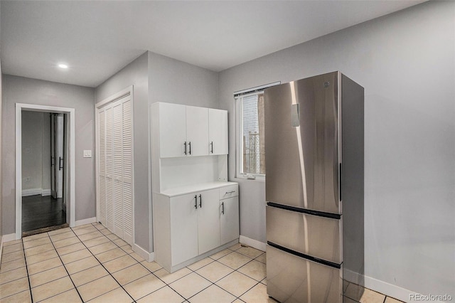 kitchen with freestanding refrigerator, white cabinets, light countertops, baseboards, and light tile patterned floors