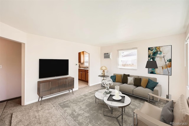 living area with arched walkways, baseboards, light carpet, and a wall mounted air conditioner