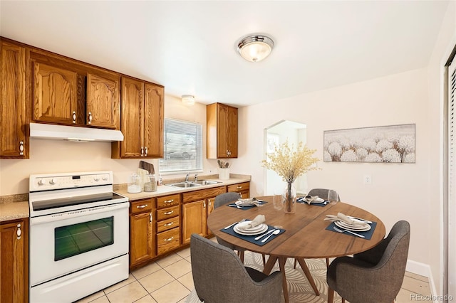 kitchen featuring under cabinet range hood, white range with electric cooktop, brown cabinets, and a sink