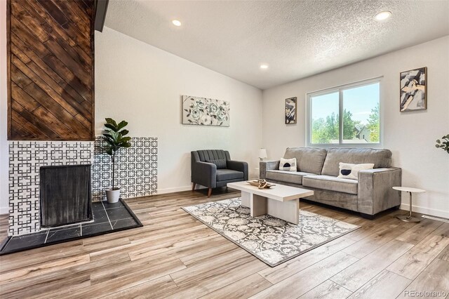 17979 E Oxford Pl, Aurora, CO 80013 - living area featuring vaulted ceiling, wood finished floors, a textured ceiling, baseboards, and a tiled fireplace