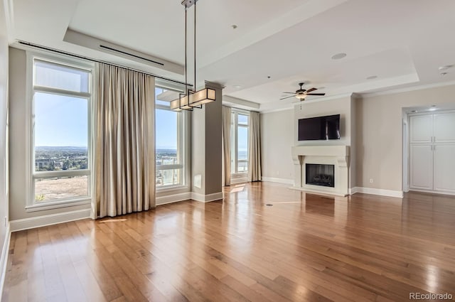 unfurnished living room featuring ceiling fan, hardwood / wood-style flooring, a tray ceiling, and ornamental molding