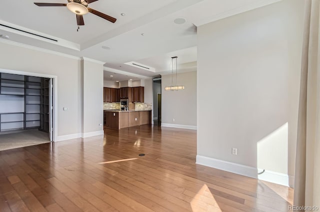 unfurnished living room with ceiling fan, hardwood / wood-style flooring, a tray ceiling, and crown molding