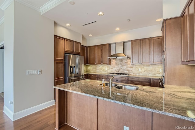 kitchen featuring appliances with stainless steel finishes, wall chimney exhaust hood, kitchen peninsula, stone counters, and sink