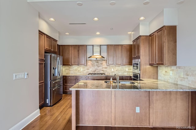 kitchen featuring wall chimney exhaust hood, kitchen peninsula, appliances with stainless steel finishes, and sink