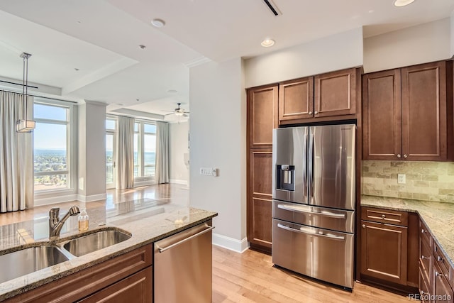 kitchen featuring appliances with stainless steel finishes, light stone counters, light hardwood / wood-style flooring, decorative light fixtures, and sink