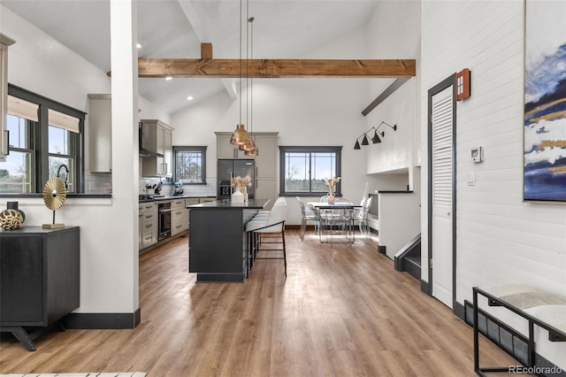 kitchen featuring a breakfast bar, beam ceiling, gray cabinets, stainless steel refrigerator with ice dispenser, and dark countertops