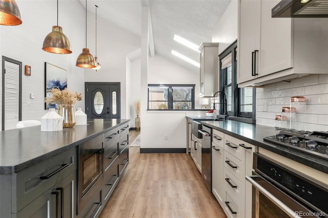 kitchen with a sink, ventilation hood, light wood-style floors, appliances with stainless steel finishes, and decorative backsplash