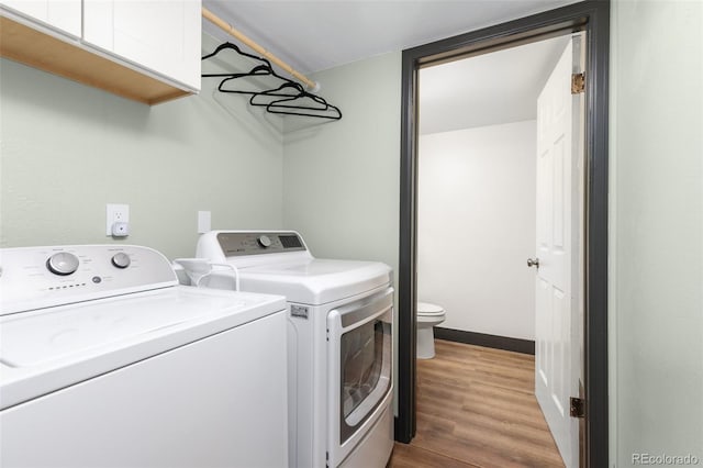 clothes washing area featuring wood finished floors, cabinet space, independent washer and dryer, and baseboards